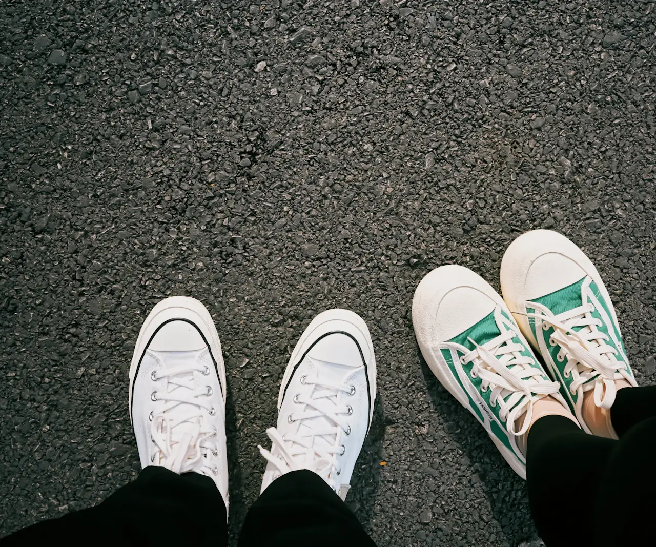 Deux paires de baskets en toile, blanches et vertes, vues d'en haut sur le bitume d'une rue