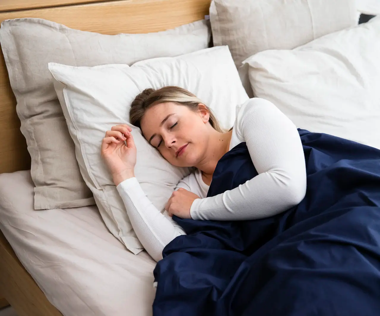 Jeune femme endormie dans un lit aux draps clairs, sous une couette bleu marine