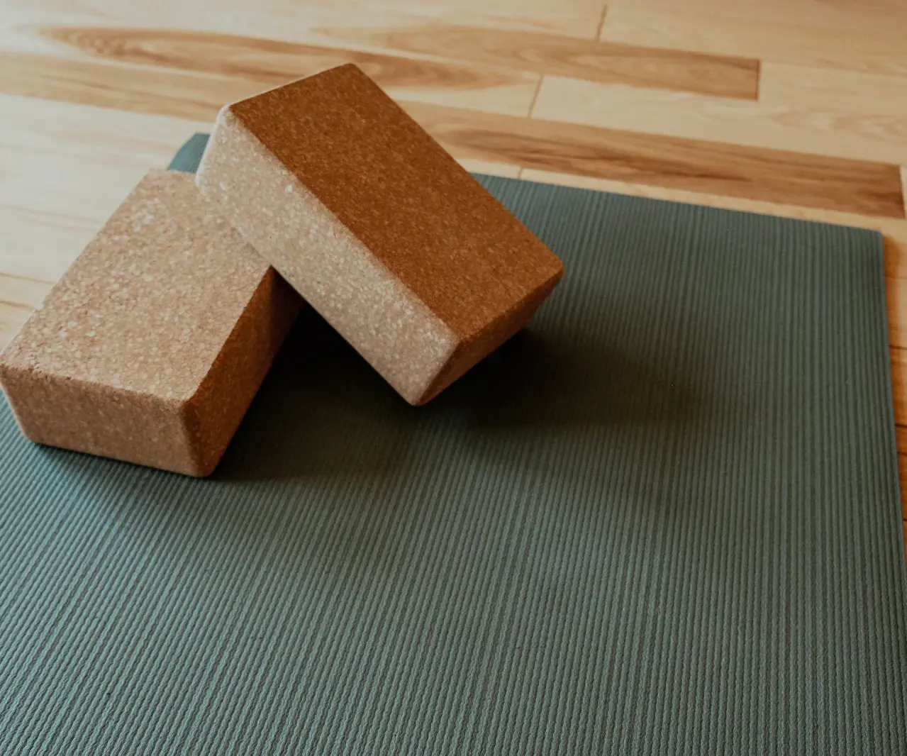 Tapis de yoga vert sauge avec deux briques en liège posées sur un parquet