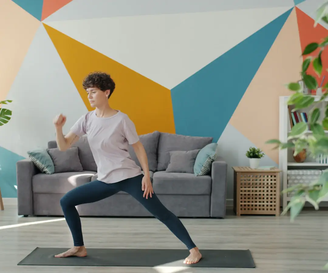 Femme en fente sur un tapis de sport dans un salon aux murs colorés, devant un canapé gris