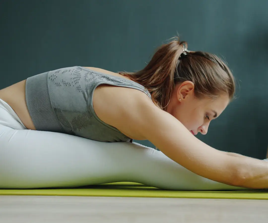 Femme assise sur un tapis vert qui s'étire vers ses pieds, jambes tendues