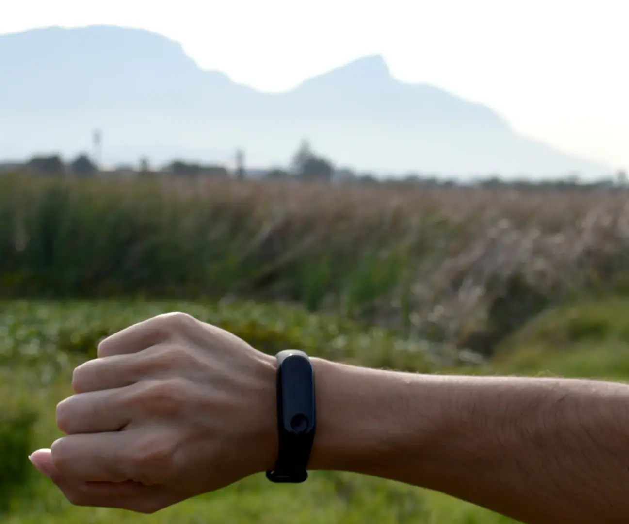 Homme qui regarde le bracelet connecté noir à son poignet, en pleine nature, avec des montagnes au loin