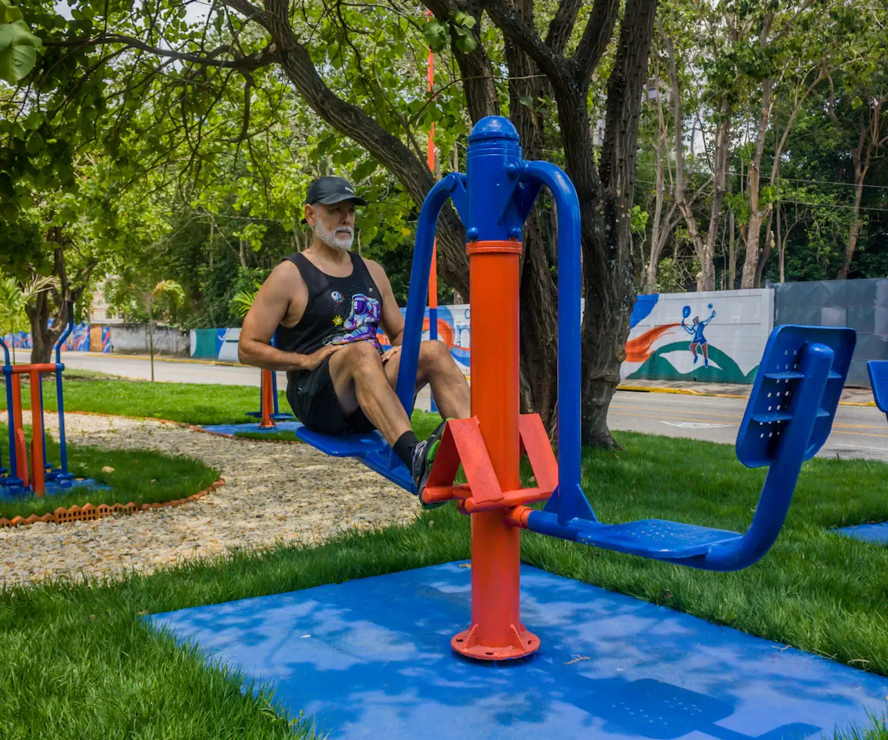 Homme à la barbe grise en débardeur faisant un exercice d'abdominaux sur un appareil de fitness en plein air, dans un parc arboré