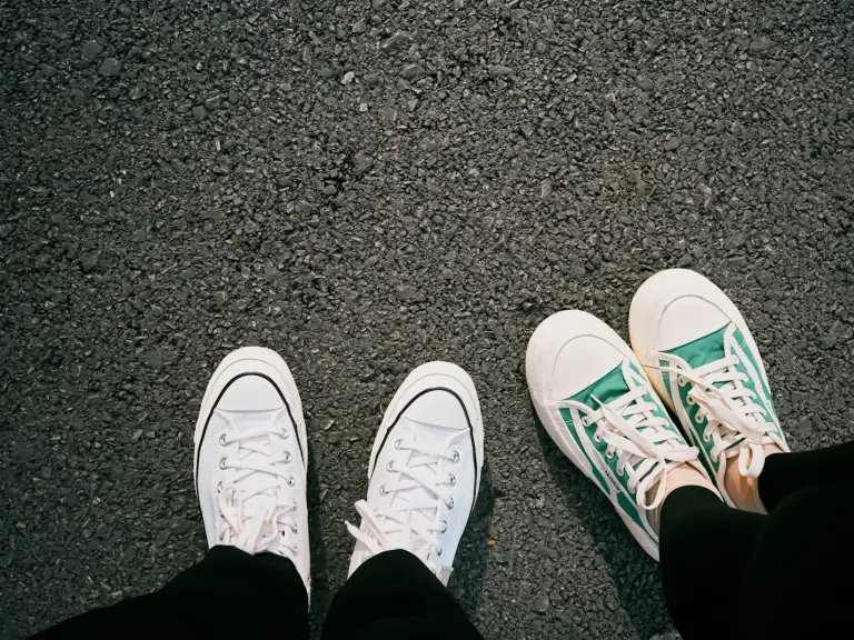 Deux paires de baskets en toile, blanches et vertes, vues d'en haut sur le bitume d'une rue