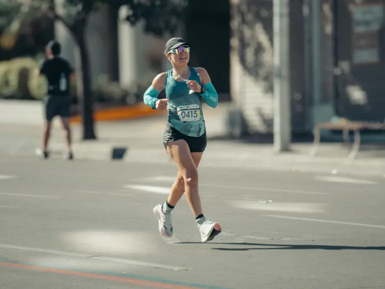 Coureuse souriante en débardeur turquoise et lunettes de soleil pendant une course sur route ensoleillée