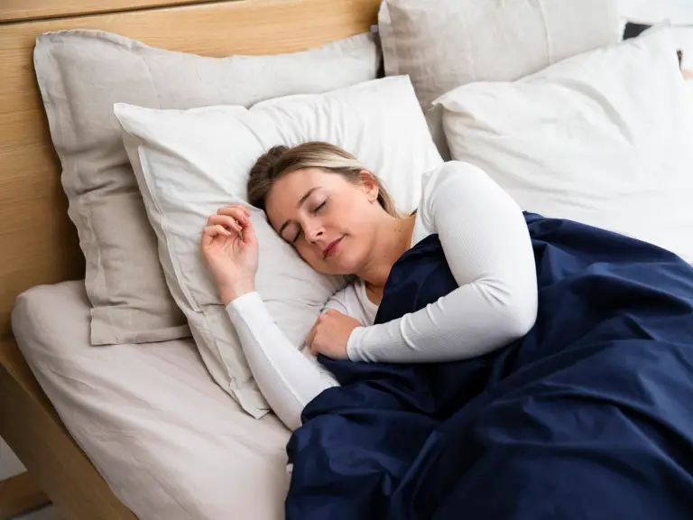 Jeune femme endormie dans un lit aux draps clairs, sous une couette bleu marine