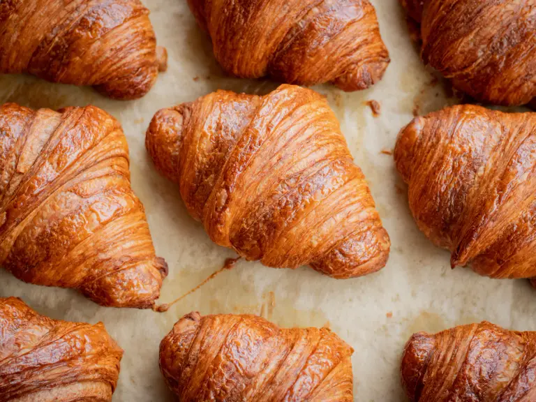 Plaque de croissants dorés tout juste sortis du four, alignés sur du papier cuisson