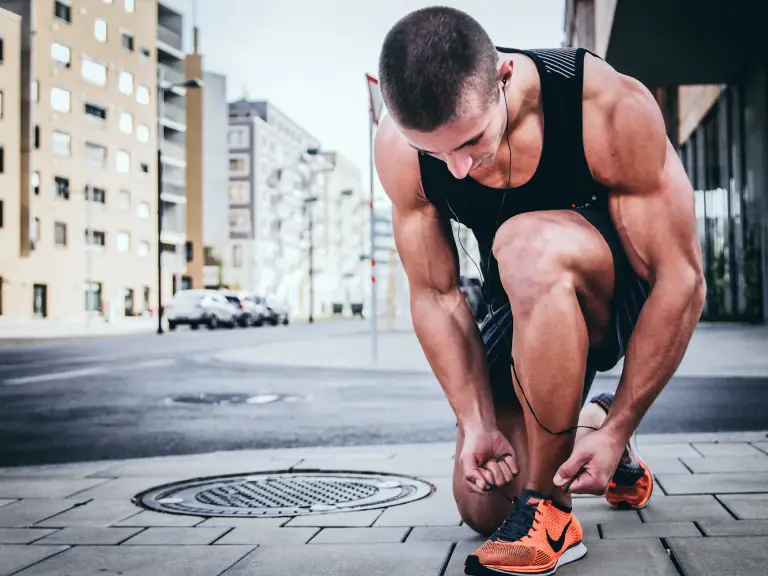 Coureur accroupi sur un trottoir en ville qui lace ses chaussures de running orange avant de partir courir