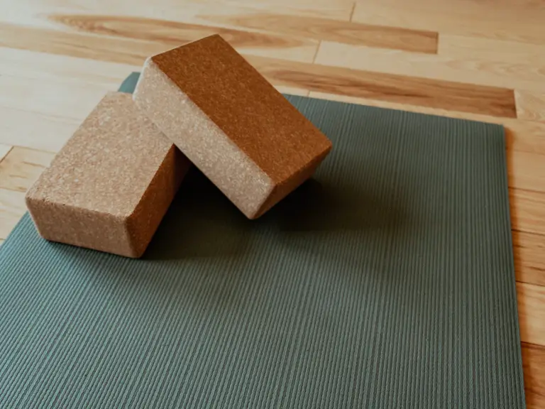 Tapis de yoga vert sauge avec deux briques en liège posées sur un parquet