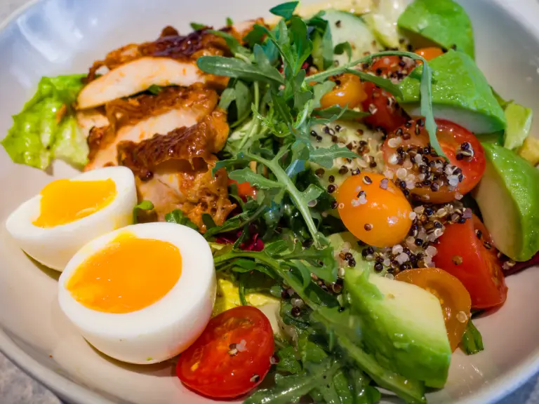 Bol de salade avec poulet grillé tranché, deux demi-oeufs mollets, avocat, tomates cerises, roquette et quinoa
