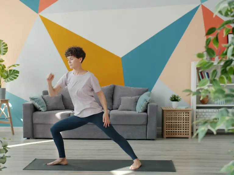Femme en fente sur un tapis de sport dans un salon aux murs colorés, devant un canapé gris