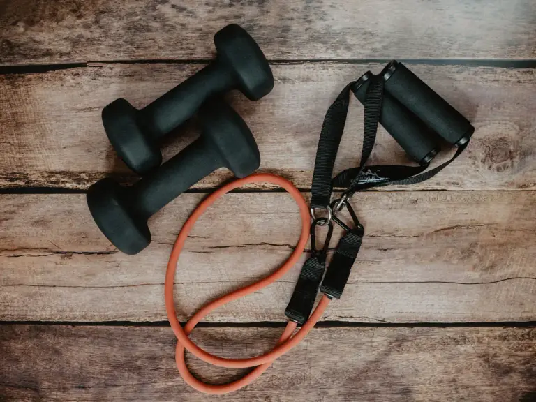 Élastique tubulaire orange à poignées noires posé à côté de deux haltères noirs sur un plancher en bois brut