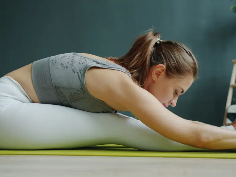 Femme assise sur un tapis vert qui s'étire vers ses pieds, jambes tendues