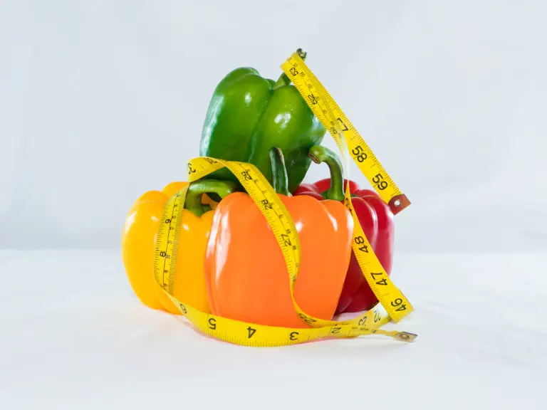 Trois poivrons vert, jaune, orange et rouge entourés d'un mètre ruban jaune sur fond blanc
