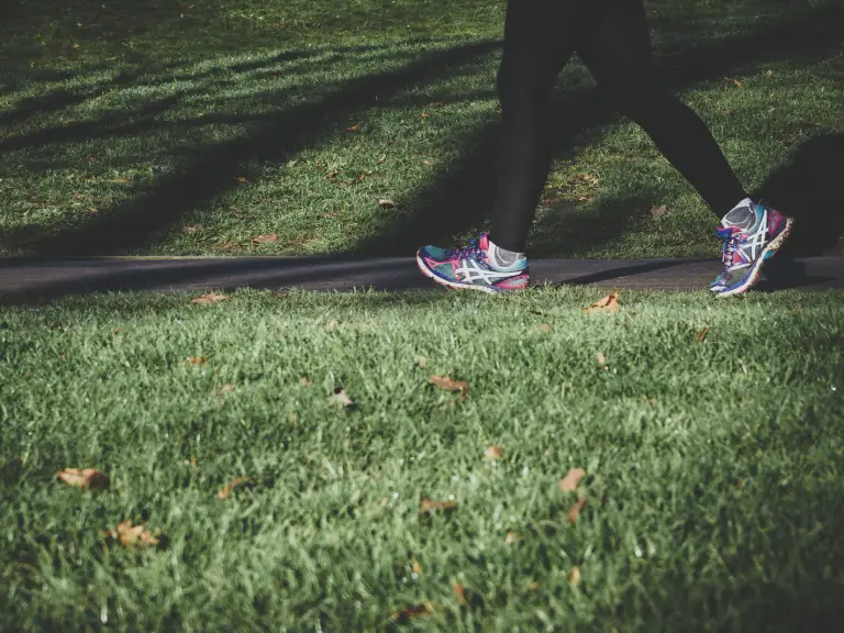 Jambes d'une personne en baskets colorées marchant d'un bon pas sur une allée entre deux pelouses