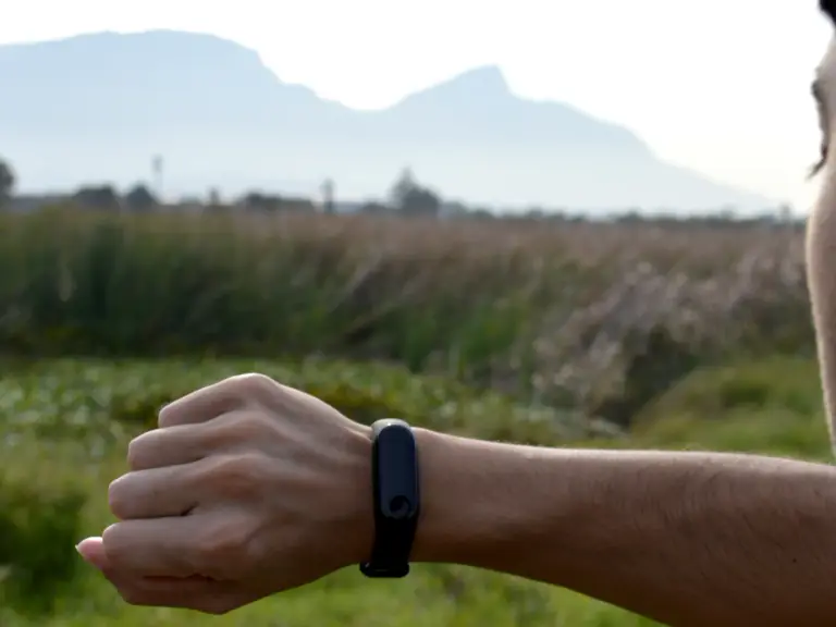 Homme qui regarde le bracelet connecté noir à son poignet, en pleine nature, avec des montagnes au loin