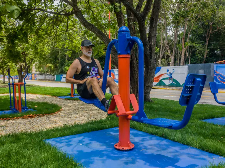 Homme à la barbe grise en débardeur faisant un exercice d'abdominaux sur un appareil de fitness en plein air, dans un parc arboré
